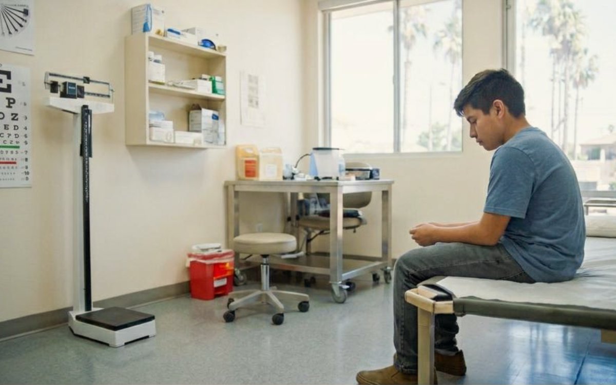 Student sitting alone on a cot in an empty school health office