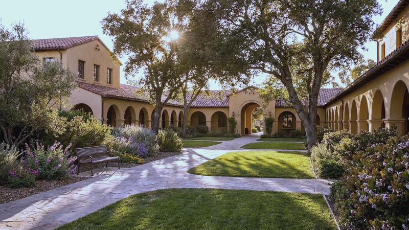 Mission-style courtyard with arched arcades and oak trees in late-afternoon light
