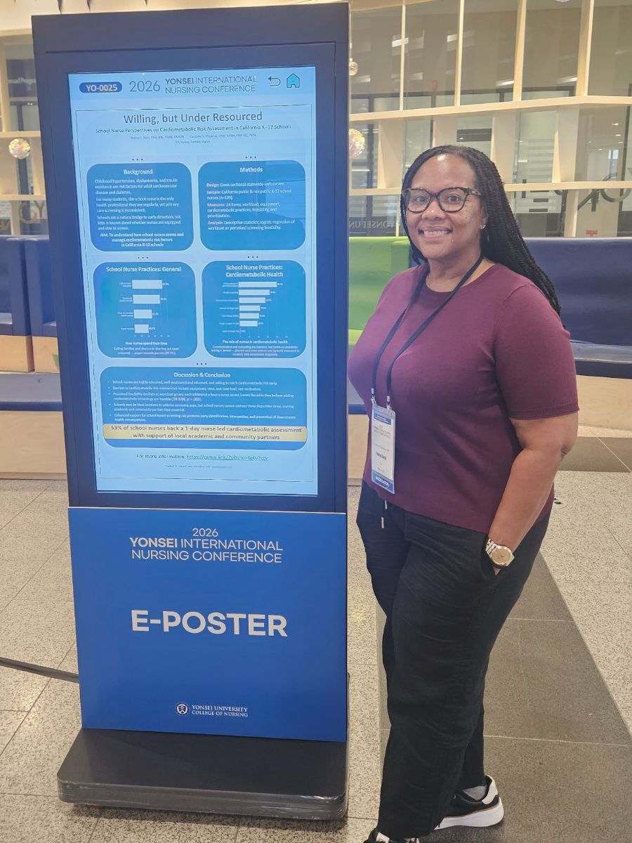 Nakia Best standing beside the e-poster kiosk displaying Willing, but Under Resourced