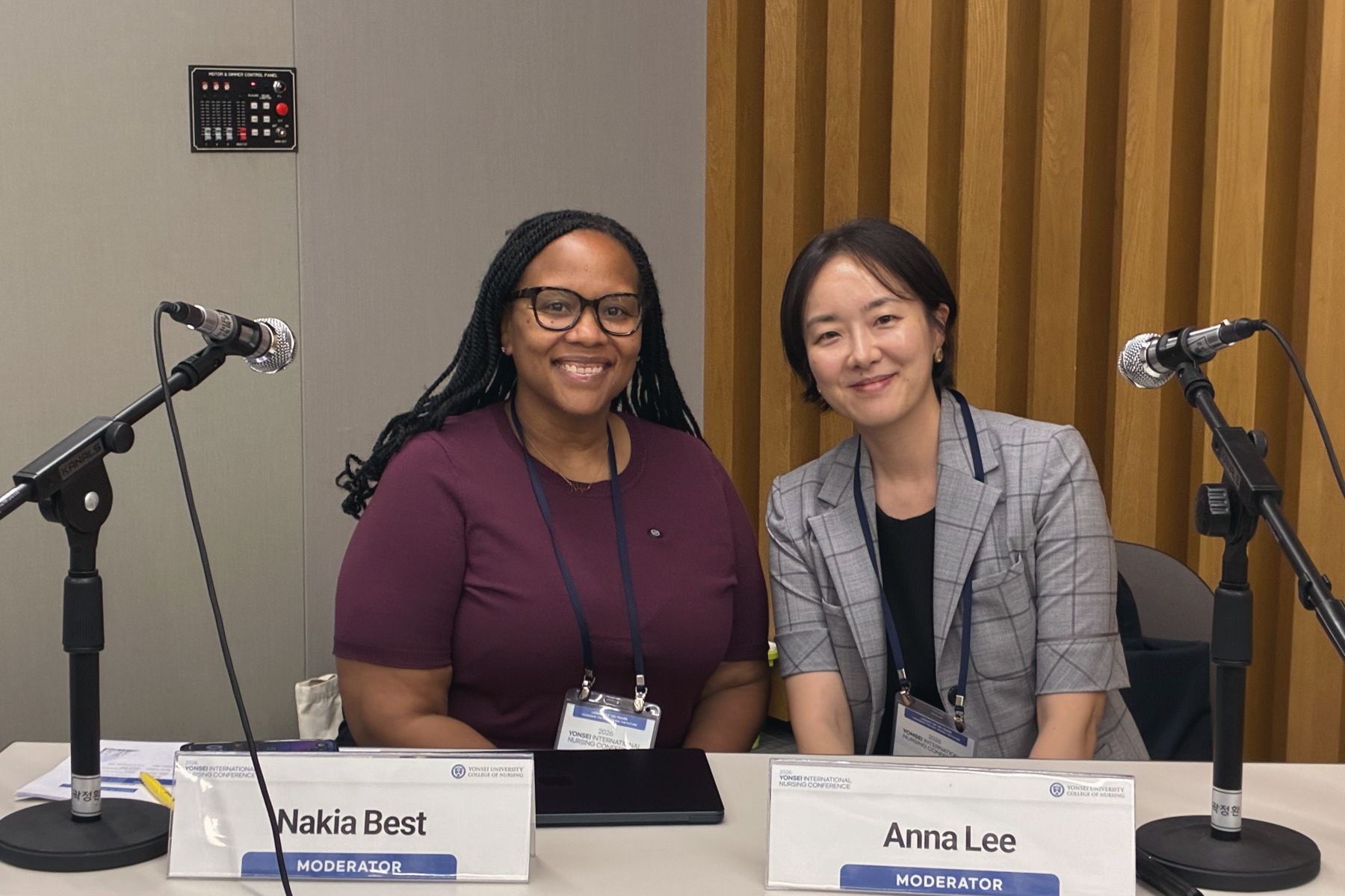 Nakia Best and Anna Lee seated at the moderator table with name cards and microphones